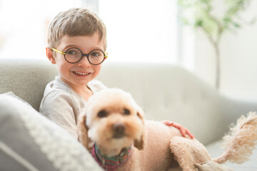 portrait of handsome little boy in glasses sit on sofa with dog © Louis-Paul Photo