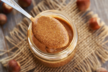 Homemade hazelnut butter on a spoon above a glass jar