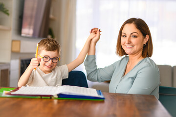homework and school concept - smiling student boy with book writing to notebook at home with his...