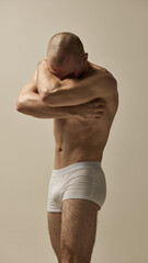 Bare-chested man, model dressed white underwear, covering face with arm in introspective pose...