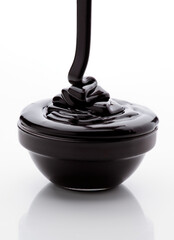 Rich chocolate sauce drizzles elegantly from a spoon into a smooth, dark bowl