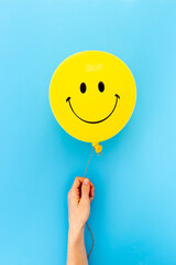 Happy smiling yellow balloon in hand. Happiness emotions concept © 9dreamstudio