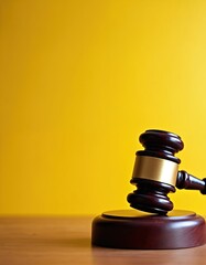 Close-up of wooden gavel resting on sound block. Justice symbol on vivid yellow background. Dark wood, gold colors. Law, legal system, attorney work, court decisions, order, right to defend.