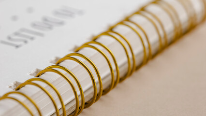 Close up shot of a spiral notebook. The pages are white and the spirals are gold. The notebook...