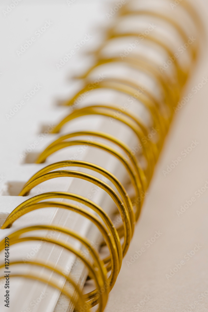 Poster close-up of a notebook's gold spiral binding and blank white pages, a simple yet elegant design, per