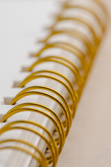 Close-up of a notebook's gold spiral binding and blank white pages, a simple yet elegant design,...