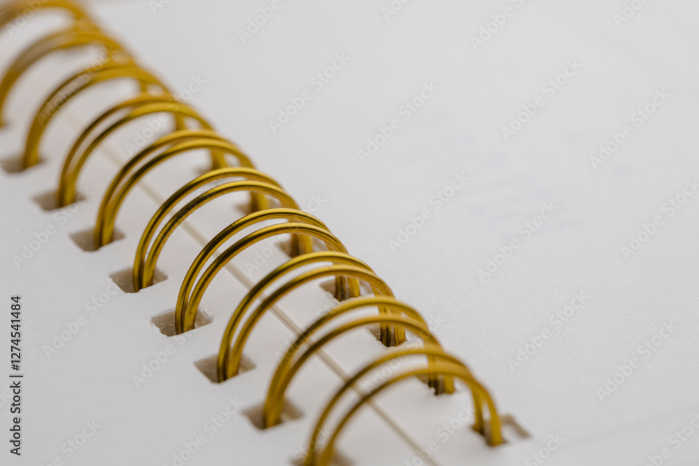 Poster close-up view of a notebook bound with a gold spiral binding. the paper is bright white and smooth, 