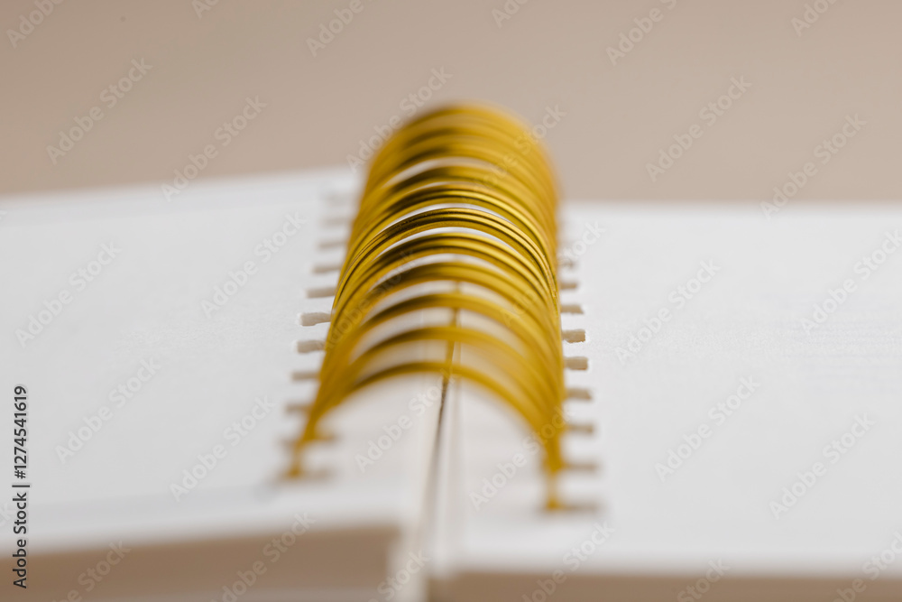 Poster close-up of spiral notebook with gold wire binding. clean, white pages create a minimalist aesthetic