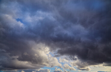 Obraz premium Storm clouds with glimpses of sunlight against the deep blue sky. The dramatic contrast of dark masses and bright rays gives the shot a unique expressiveness.