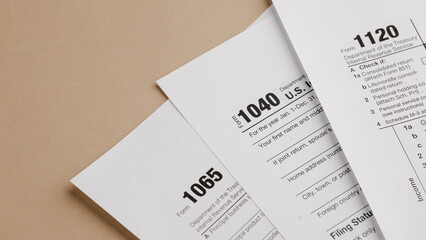 Obraz premium Tax Form Documents: A close-up view of various tax forms including 1040, 1065, and 1120, placed on a neutral-toned surface, ready for completion and filing.