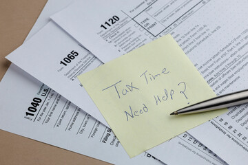 Tax season stress: Forms, sticky note reminder for help, and a pen suggest financial complexities and the need for assistance.