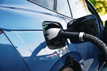 Electric vehicle charging at a public station on a sunny day in a busy urban area