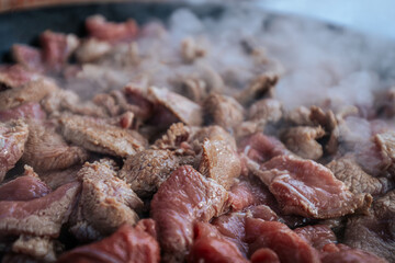 Freshly sliced beef is sizzling in a hot pan, with steam rising as the meat cooks. The mixture of raw and browned pieces highlights the cooking process and the release of rich flavors.