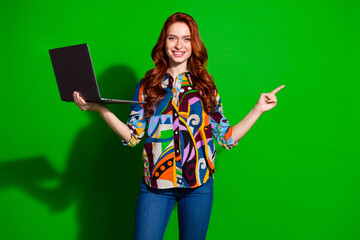Young stylish woman with long red hair smiling and gesturing while holding laptop against vibrant...