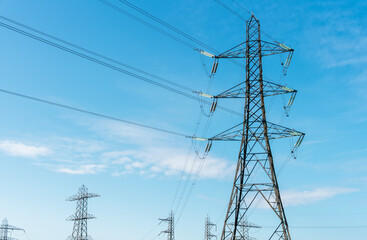 High voltage power lines stretch across bright blue sky in an open landscape