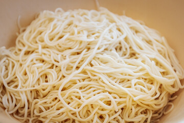A close-up of freshly cooked noodles in a white bowl. The soft, slightly glossy texture highlights their perfect preparation, ready to be served or mixed with other ingredients.