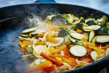 A steaming vegetable stir-fry with zucchini, bell peppers, carrots, and broccoli is being cooked in a pan. A spatula is stirring the fresh, colorful ingredients.