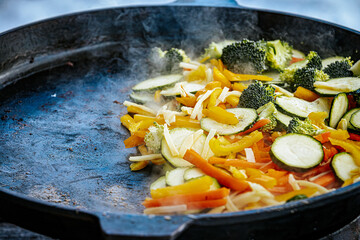 A steaming vegetable stir-fry with zucchini, bell peppers, carrots, and broccoli is being cooked in...
