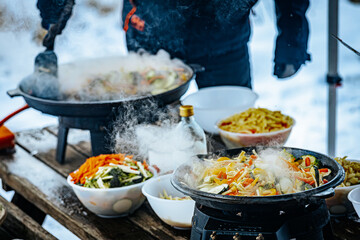 A steaming vegetable stir-fry with zucchini, bell peppers, carrots, and broccoli is being cooked in a pan. A spatula is stirring the fresh, colorful ingredients.
