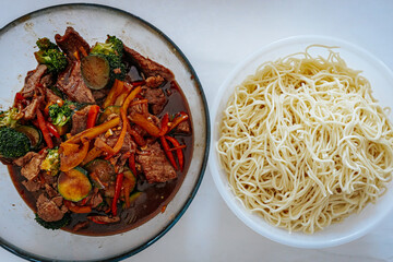 A delicious beef stir-fry with colorful vegetables in a savory sauce, served alongside a bowl of cooked noodles. A flavorful Asian-inspired meal ready to be enjoyed.