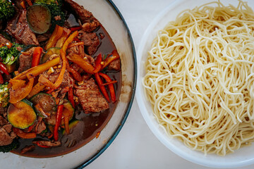 A delicious beef stir-fry with colorful vegetables in a savory sauce, served alongside a bowl of cooked noodles. A flavorful Asian-inspired meal ready to be enjoyed.