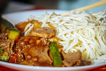 A close-up of a plate of stir-fried beef with vegetables, served with noodles. A person is using chopsticks to enjoy this flavorful Asian-inspired dish.