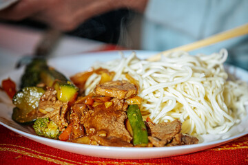A close-up of a plate of stir-fried beef with vegetables, served with noodles. A person is using chopsticks to enjoy this flavorful Asian-inspired dish.
