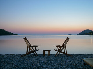 Sunset silhouettes of two wooden empty chairs on the beach