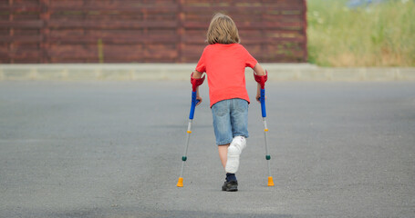 Kid with broken leg in plaster cast, walking with medical orthopedic crutches