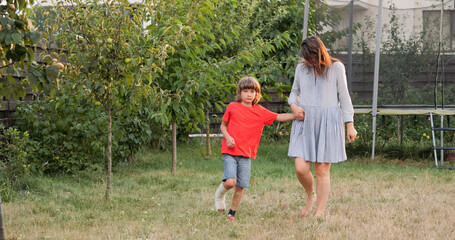 Kid with leg in cast helped by his mother to walk limping in the garden