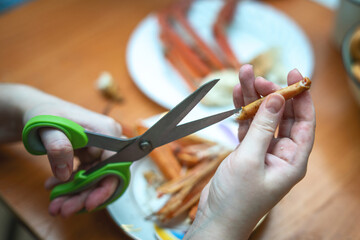 hand using scissors to cut a segment of a cooked crab's limb to extract the meat. The image captures the intricate process of seafood preparation