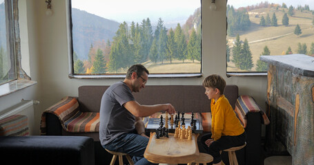 Father and son play chess in a rustic mountain chalet