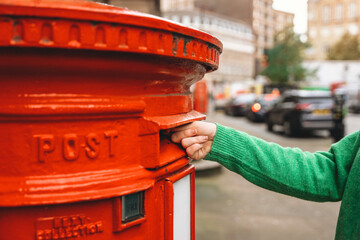 Bright red mailbox with hand inserting letter on busy city street in autumn