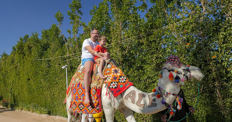Obraz premium Father and little son ride a camel in Hurghada touristic resort