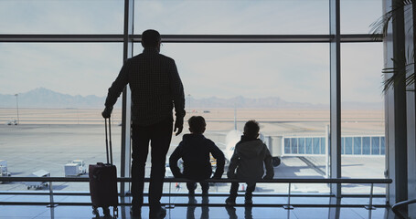 Man with suitcase and his kids wait in airport to board on their flight