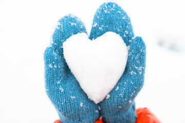 Person in colorful mittens holds a heart-shaped snowball in a winter landscape