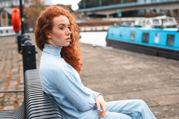 Young woman sits by canal in city, enjoying leisure time and contemplating life