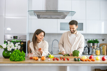 A joyful couple shares culinary moments while preparing fresh ingredients in a beautifully styled kitchen for a delicious meal.