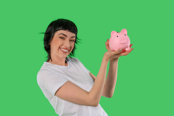 Smiling woman holds pink piggy bank against bright green background in creative studio