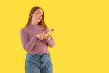 Young woman engaged with smartphone against bright yellow background