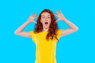 Fototapeta premium Excited young woman with curly hair poses in bright yellow shirt against blue background