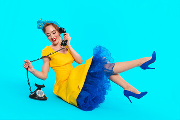 Woman in yellow dress with blue accents poses with vintage phone on bright blue background