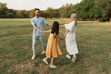 Family holding hands and playing joyfully in a beautiful green park.