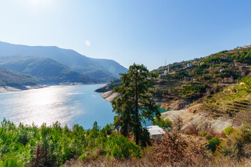 Beautiful natural landscape showcasing a peaceful lake with surrounding forested hills and a mosque in the background.