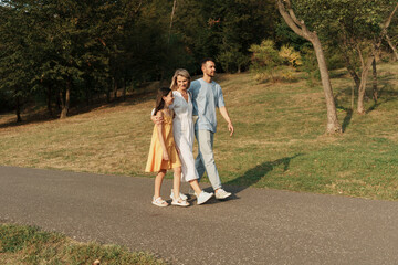 A family of three walking happily in a park on a sunny day.