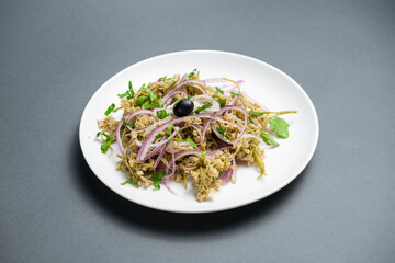 Flavorful dish of shredded meat garnished with onions, herbs, and olives presented on a white plate in a minimalist setting