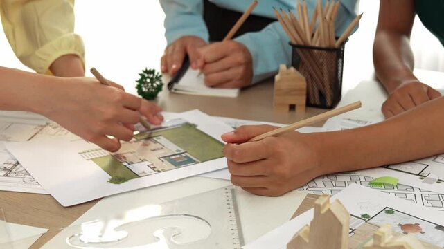 Smart architect and safety engineer discussion about building blueprint on table with architectural document, measurement tools and wooden block scatter around at modern office. Closeup. Delineation.