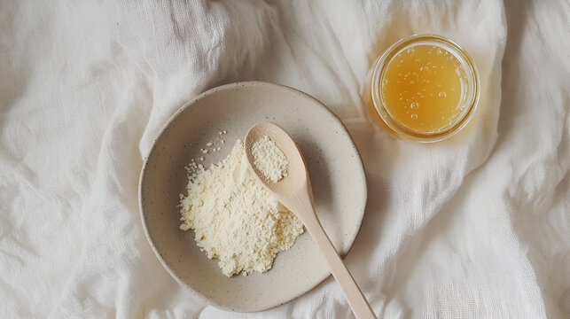 Golden honey, powder, and wooden spoon on soft white cloth, creating a minimal, soothing, natural aesthetic.