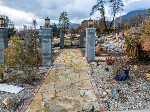 Burned sedan in the driveway of a home destroyed by the Eaton Fire in Altadena, California, with surviving entry pillars highlighting the aftermath of a devastating urban wildfire
