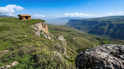 A small wooden cabin sits atop a high plateau, offering breathtaking views of the deep valley and distant mountains under clear skies